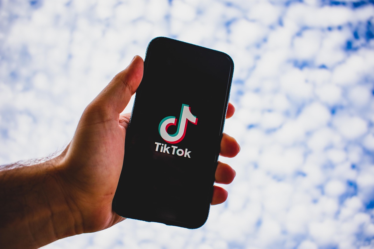 aplikasi tiktok dalam handphone digenggam dengan latar langit